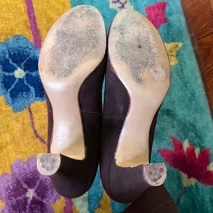 May include: A pair of brown suede heeled shoes with a light brown sole. The shoes are on a patterned rug.