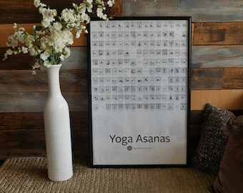 May include: A black framed poster with a white background and the text "Yoga Asanas" in black. The poster features a grid of black and white images of yoga poses. The poster is hanging on a wooden wall with a white vase and white flowers in front of it.