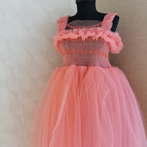 K&ouml;nnte beinhalten: Korallfarbenes Kleid auf einer schwarzen Schaufensterpuppe. Das Kleid hat ein eng anliegendes Oberteil mit orangefarbenen N&auml;hten und einen mehrlagigen T&uuml;llrock. Die Tr&auml;ger und der Ausschnitt sind mit R&uuml;schenstoff verziert.