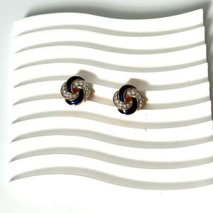 May include: A pair of gold tone earrings with a blue enamel and clear rhinestone knot design.