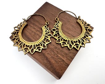 May include: A pair of gold-toned hoop earrings featuring an intricate, openwork filigree design with a scalloped edge. The earrings have a circular inner opening and a thin wire closure mechanism, showcasing a detailed, symmetrical pattern.