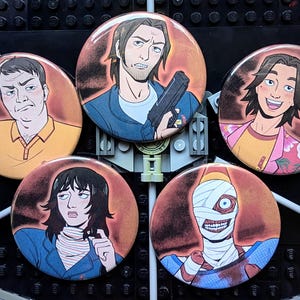 Peut inclure: Ensemble de cinq badges ronds représentant des illustrations de personnages de dessins animés. Les badges présentent différents personnages avec diverses expressions et poses, dont un tenant une arme et un autre faisant le signe de la paix.