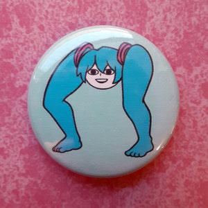 May include: A round, light blue button featuring a cartoon character with blue hair and legs. The character's hair is styled in pigtails with pink accents. The character's legs are bent, and the feet are visible at the bottom of the button.