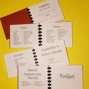 Puede incluir: Un primer plano de un libro con una cubierta blanca y texto negro. El libro se titula "Cadette" y tiene una lista de insignias y premios para ni&ntilde;as. El libro est&aacute; abierto en una p&aacute;gina con el t&iacute;tulo "Leadership in Action Awards".