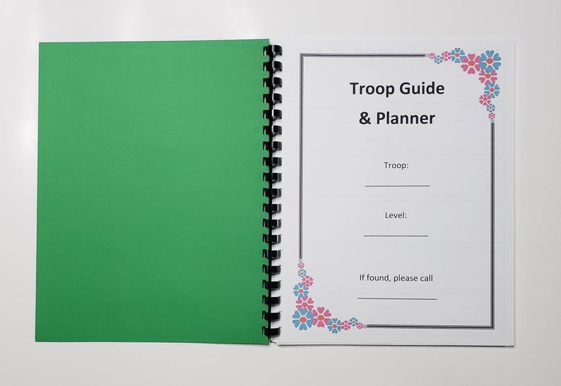 May include: Open spiral-bound notebook with a green cover and a white page with the text "Troop Guide & Planner." The page includes fill-in-the-blank lines for troop and level, and a contact request. Floral corner accents.