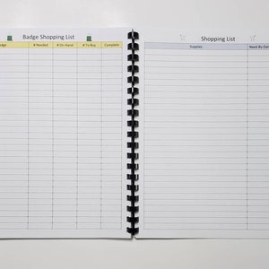 May include: Open notebook with a black spiral binding, featuring a shopping list layout. The left page is labeled "Badge Shopping List" with columns for "Badge," "Needed," "On-Hand," "To Buy," and "Complete." The right page is labeled "Shopping List" with columns for "Supplies," "Need-By-Date," and "Complete."