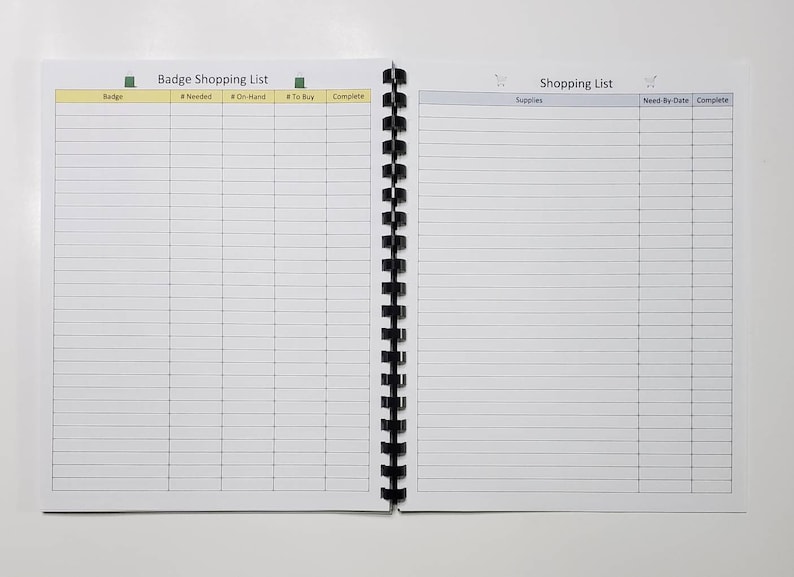 May include: Open notebook with a black spiral binding, featuring a shopping list layout. The left page is labeled "Badge Shopping List" with columns for "Badge," "Needed," "On-Hand," "To Buy," and "Complete." The right page is labeled "Shopping List" with columns for "Supplies," "Need-By-Date," and "Complete."