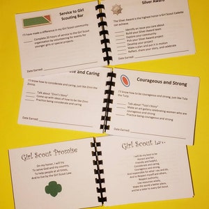 Puede incluir: Un manual de Girl Scout con una cubierta blanca y una encuadernaci&oacute;n en espiral negra. El manual incluye secciones sobre el servicio a las ni&ntilde;as, la consideraci&oacute;n y el cuidado, el coraje y la fuerza, la Promesa de Girl Scout y la Ley de Girl Scout.