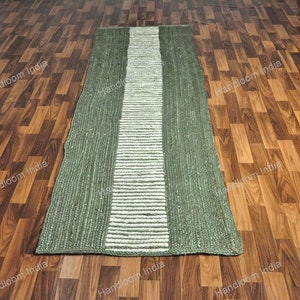 K&ouml;nnte beinhalten: Ein gr&uuml;ner und wei&szlig;er Jute-Teppich mit einem gestreiften Design. Der Teppich liegt auf einem Holzboden.