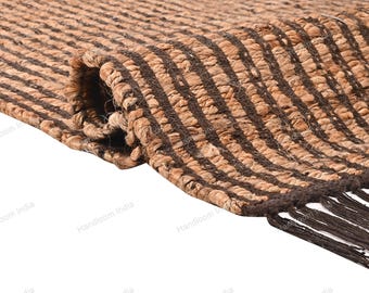 May include: A rolled-up, rectangular jute rug with a natural tan base and dark brown vertical stripes. The rug has a fringed edge and the text "Handloom India" is visible along the bottom edge.