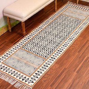 Peut inclure: Tapis à motifs noirs et blancs avec une bordure à franges. Le tapis présente un motif géométrique avec une section centrale présentant un motif plus complexe.