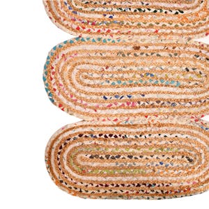 May include: Close-up of three oval-shaped jute rugs. The rugs have a natural tan color with a braided border. The centers are filled with colorful recycled fabric scraps, creating a textured, multi-colored pattern. The rugs are arranged vertically.