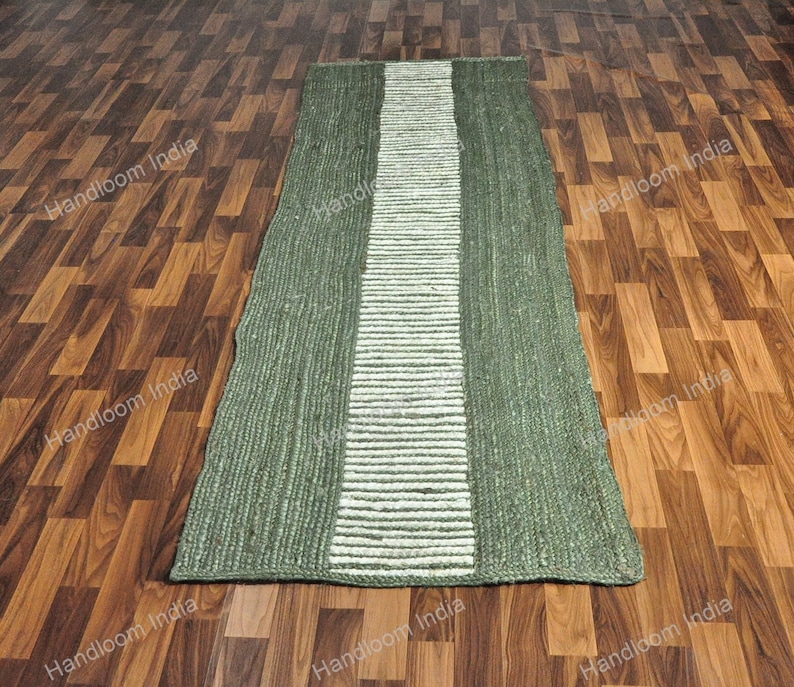 K&ouml;nnte beinhalten: Ein gr&uuml;ner und wei&szlig;er Jute-Teppich mit einem gestreiften Design. Der Teppich liegt auf einem Holzboden.