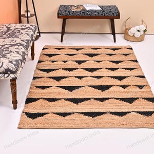 May include: A rectangular jute rug with a geometric black triangle pattern. The rug is beige with black accents and is placed on a white floor. The rug is part of a home decor collection.
