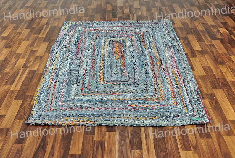 May include: A rectangular blue and multi-coloured rug made from recycled denim. The rug has a woven pattern with a central rectangle.