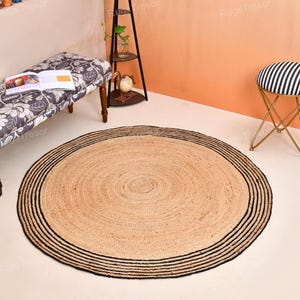May include: A round jute rug with a natural tan center and a black striped border. The rug is on a light-colored floor, with a bench, stool, and shelving unit in the background.