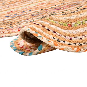 May include: Braided jute rug with a rolled edge, showcasing a mix of natural beige and colorful threads. The rug's texture is visible, with a close-up view highlighting the woven pattern and the blend of colors.