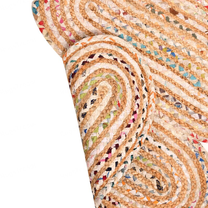May include: Close-up of a natural fiber rug with a braided design. The rug features a mix of beige, brown, and colorful recycled fabric accents. The rug is rolled up, showing the texture and pattern.