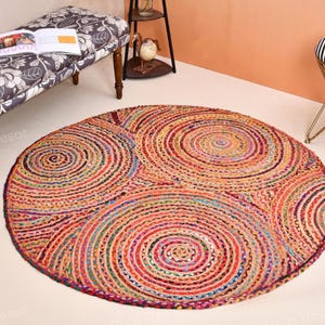 May include: A circular jute rug with a spiral pattern in various colours, including red, orange, blue, and purple. The rug is the focal point, with a bench, stool, and decorative shelf in the background.