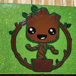 May include: A green glitter background with a brown cartoon character of Groot from Guardians of the Galaxy. Groot is smiling and has large eyes. He is standing in a brown pot and has green vines around him. The text "Follow Your Dreams" is at the bottom of the image.