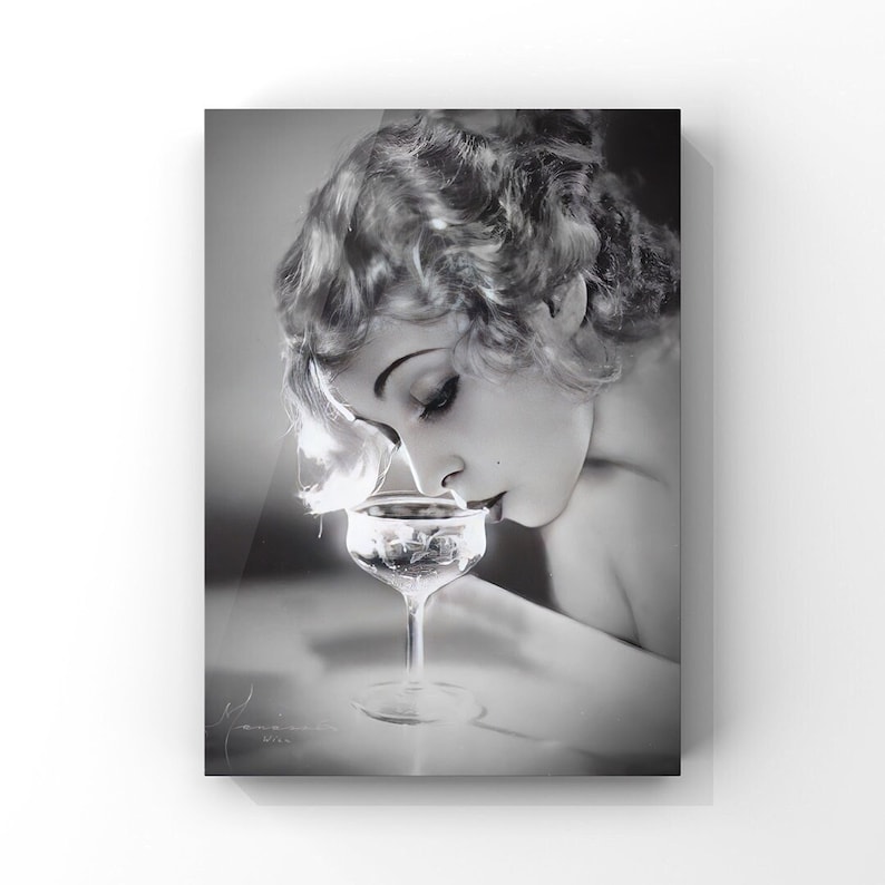 Vintage 1920s beautiful blonde flapper sipping champagne in a photograph taken by Manassé Studio. This captivating black and white image embodies the classic glamour of the Roaring 20s era, featuring an art deco aesthetic.