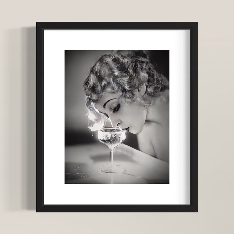 Op de afbeelding: Een zwart-witfoto van een vrouw met kort, golvend haar, die naar een champagnefluit kijkt.