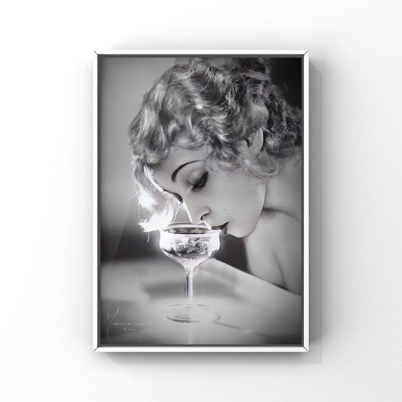 Op de afbeelding: Een zwart-witfoto van een vrouw met kort, golvend haar, die naar een glas champagne kijkt.