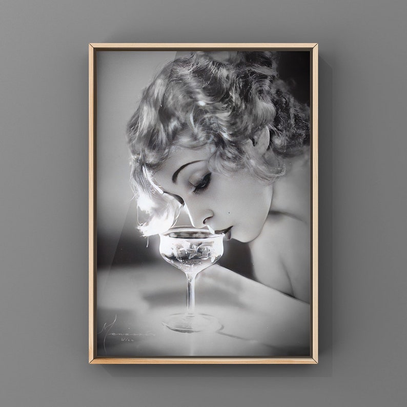 Op de afbeelding: Zwart-witfoto van een vrouw met kort, golvend haar, die naar een champagneglas met steel kijkt.
