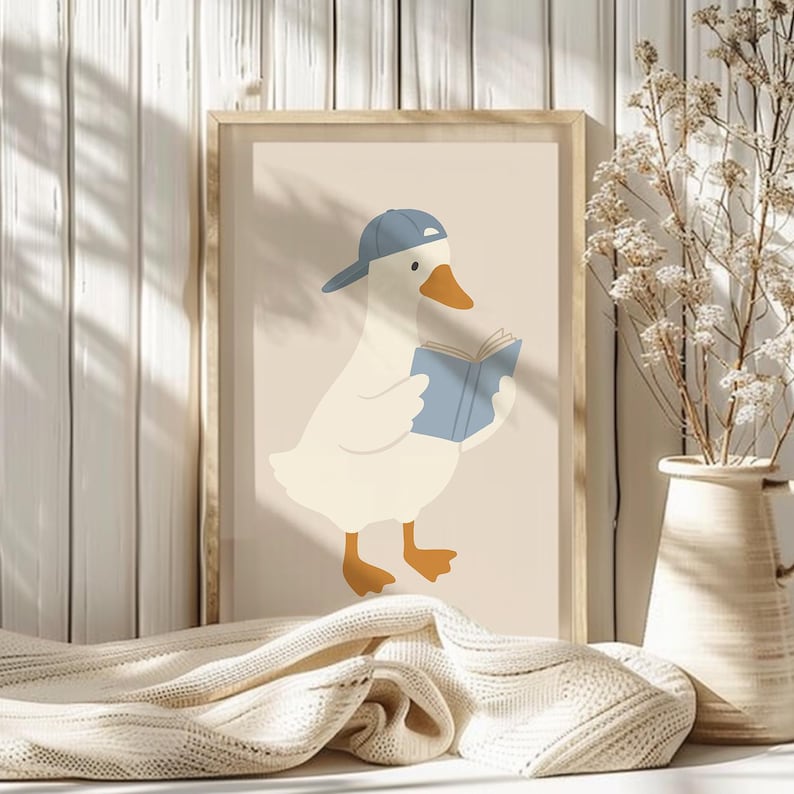 May include: A framed print featuring a cartoon goose wearing a blue baseball cap and reading a blue book. The goose is white with an orange beak and feet. The background is a light beige color.
