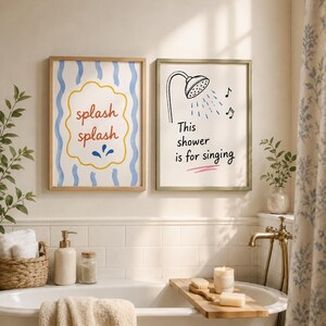 May include: Two framed wall art prints hanging above a bathtub. The left print features blue wavy lines and the red text "splash splash" inside a yellow cloud shape. The right print shows a shower head, musical notes, and the text "This shower is for singing".