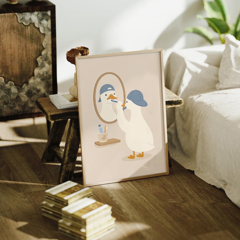 May include: A framed wall art print featuring a white duck wearing a blue baseball cap, standing in front of an oval mirror while brushing its beak with a blue toothbrush. A small shelf below the mirror holds a blue tube and a wooden toothbrush.