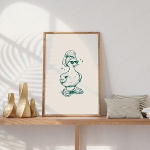 Pu&ograve; includere: Stampa incorniciata con un'anatra dei cartoni animati con occhiali da sole, un asciugamano e sandali. L'anatra &egrave; disegnata in stile linea verde su sfondo crema. La stampa &egrave; esposta su una mensola di legno.