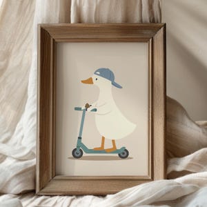 May include: A framed art print featuring a white duck wearing a blue baseball cap and riding a teal kick scooter. The illustration is set against a light beige background and is enclosed in a simple, rectangular wooden frame with a natural finish.