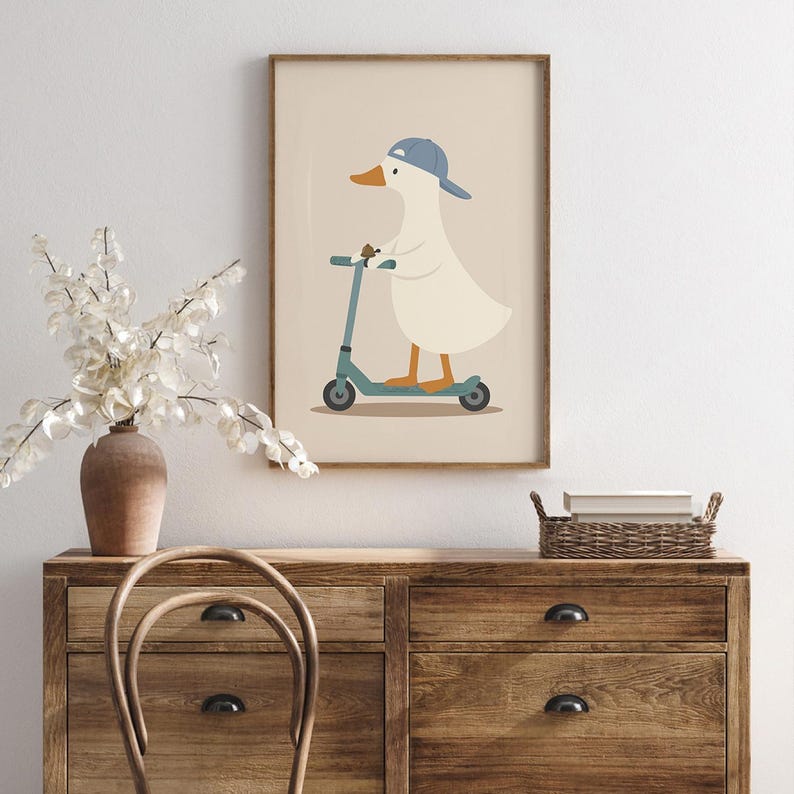 May include: A framed wall art print featuring a white duck with an orange beak and feet, wearing a blue baseball cap. The duck is standing on a teal kick scooter against a solid light beige background. The illustration is simple and graphic.