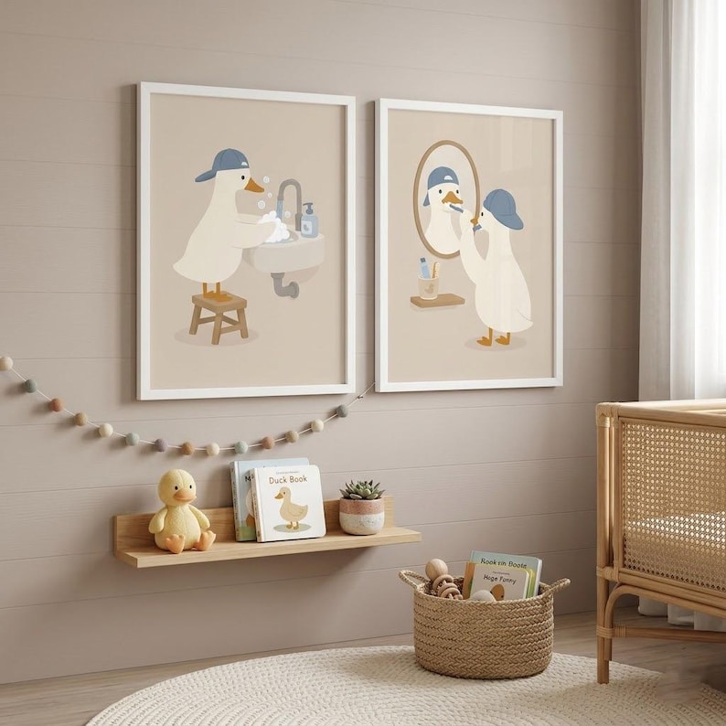 May include: Two framed wall art prints featuring a white duck wearing a blue baseball cap. One print shows the duck washing hands at a sink, while the other shows the duck brushing teeth in front of a mirror. Both prints have a light beige background.