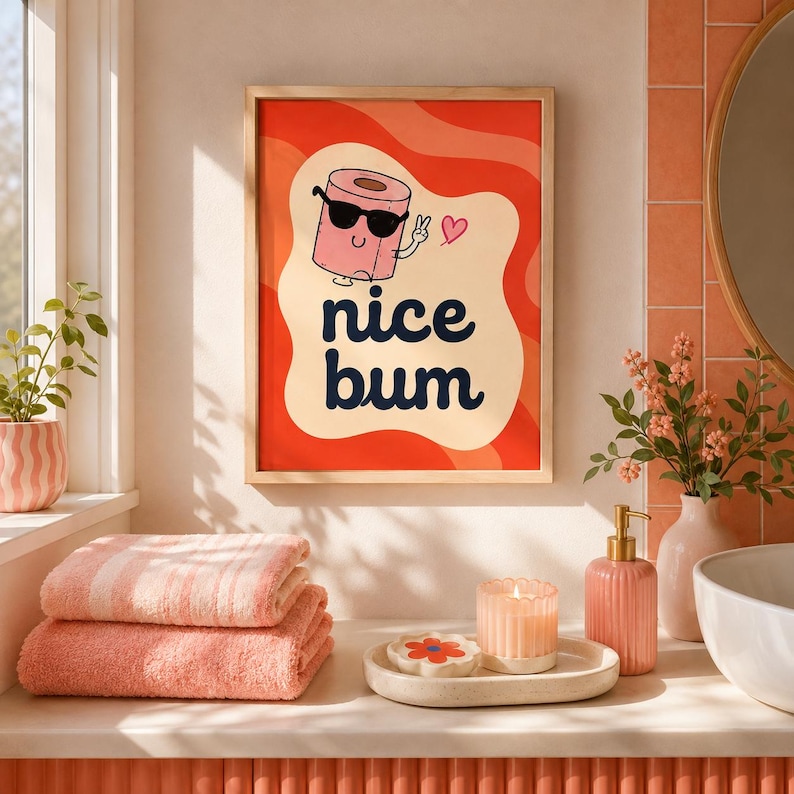 Op de afbeelding: Een rechthoekige wandprint in een lichthouten lijst met een cartoon wc-rol die een zwarte zonnebril draagt en een vredesteken maakt. De tekst "nice bum" staat in donkerblauw gedrukt tegen een golvende rode en cr&egrave;mekleurige achtergrond.