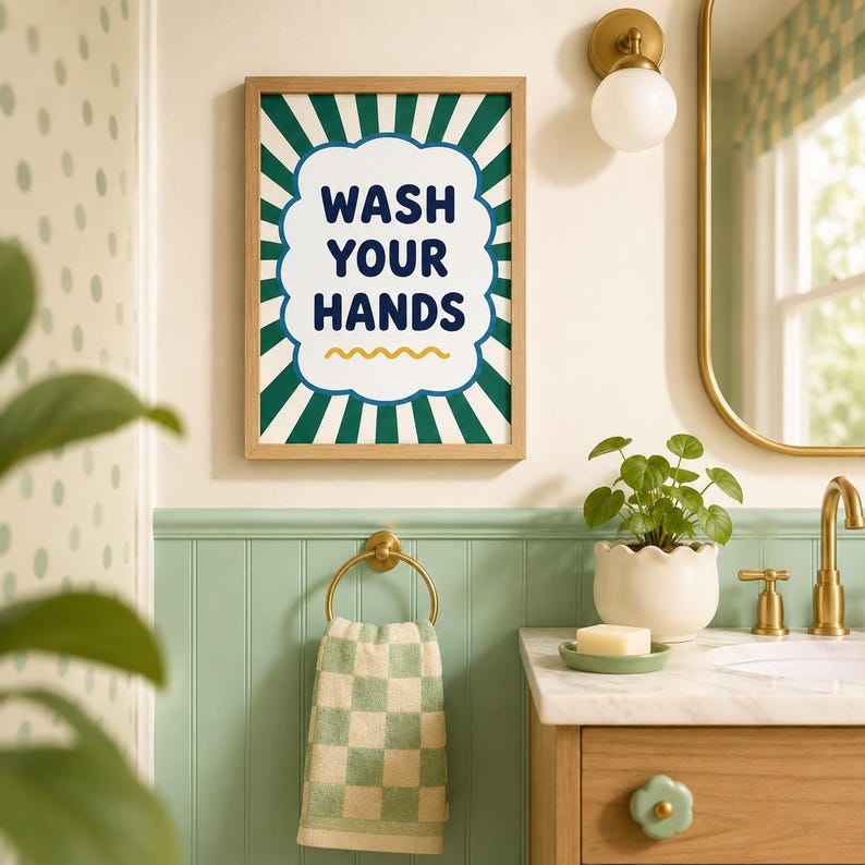 Op de afbeelding: Een rechthoekige wandkunstprint in een lichthouten lijst met een wit geschulpt middenstuk met de donkerblauwe tekst WASH YOUR HANDS en een gele golvende lijn, tegen een achtergrond van donkergroene en witte zonnestralen.