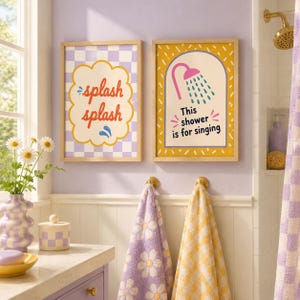 Op de afbeelding: Twee ingelijste wandprints met lichte houten lijsten. De linker print heeft een paars-witte geblokte achtergrond met de tekst "splash splash" in het rood. De rechter print heeft een gele achtergrond met een douche-icoon en de tekst "This shower is for singing" in het zwart.