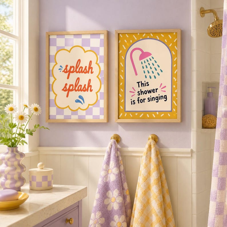 Op de afbeelding: Twee ingelijste wandprints met lichte houten lijsten. De linker print heeft een paars-witte geblokte achtergrond met de tekst "splash splash" in het rood. De rechter print heeft een gele achtergrond met een douche-icoon en de tekst "This shower is for singing" in het zwart.