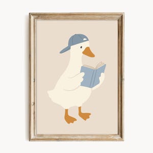 May include: A framed print featuring a cartoon goose wearing a blue baseball cap and reading a blue book. The goose is white with orange feet and a beak, set against a beige background. The frame is a light brown color.