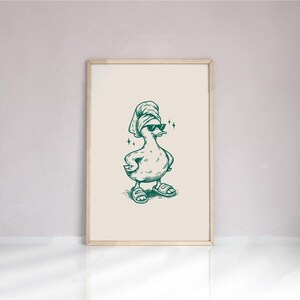 Pu&ograve; includere: Stampa incorniciata di un'anatra dei cartoni animati con occhiali da sole, asciugamano e sandali. Il disegno &egrave; realizzato con inchiostro verde su sfondo crema, incorniciato in una cornice di legno chiaro. Una divertente decorazione murale.