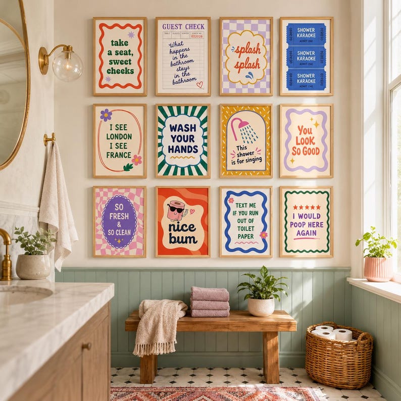 Op de afbeelding: Een galerijmuur met twaalf ingelijste kunstprints met badkamerthema, voorzien van kleurrijke typografie en illustraties, waaronder teksten zoals Take a seat, sweet cheeks, Guest Check, Splash splash, Shower Karaoke en I would poop here again.