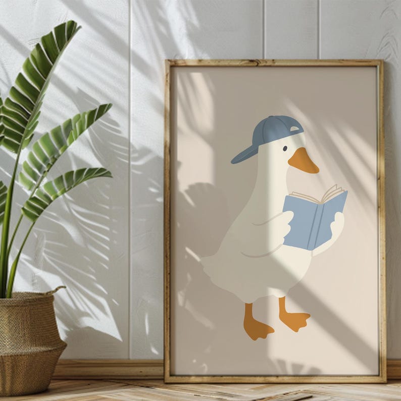May include: A framed art print featuring a cartoon goose wearing a blue baseball cap and reading a blue book. The goose has orange feet and a yellow beak. The background is a light beige color, and the frame is made of wood.