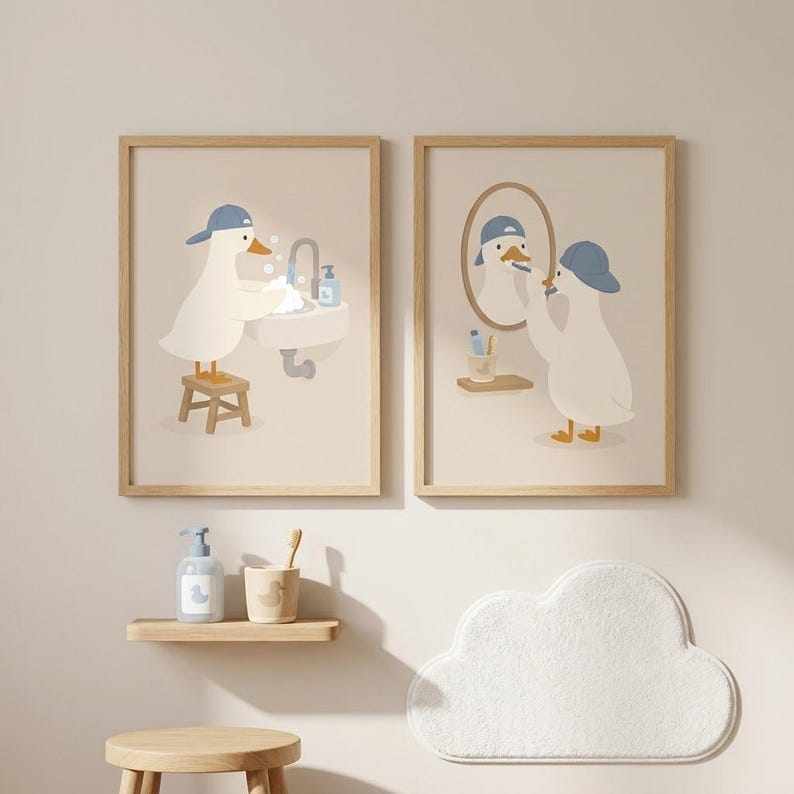 May include: Two framed wall art prints featuring a white duck wearing a blue baseball cap. The left print shows the duck washing hands at a sink on a stool. The right print shows the duck brushing teeth in front of a mirror. Below are a soap dispenser, a toothbrush holder, a wooden stool, and a cloud-shaped rug.