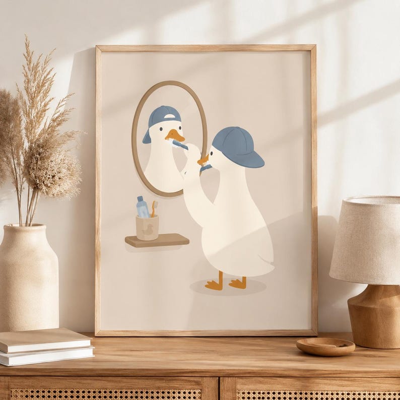 May include: A framed wall art print featuring a white duck wearing a blue baseball cap, standing before an oval mirror while brushing its beak with a toothbrush. A small shelf holds a blue bottle and a toothbrush in a cup with a duck silhouette.