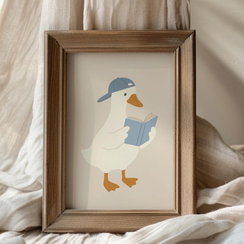 May include: A framed print featuring a cartoon goose wearing a blue baseball cap and reading a blue book. The goose has white feathers, an orange beak and feet. The frame is made of light brown wood.