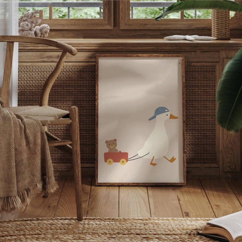 Pode incluir: Impress&atilde;o emoldurada com um pato de desenho animado usando um bon&eacute; azul, puxando uma carro&ccedil;a vermelha com um ursinho de pel&uacute;cia. A obra de arte tem um fundo neutro e uma moldura de madeira, ideal para um quarto infantil.