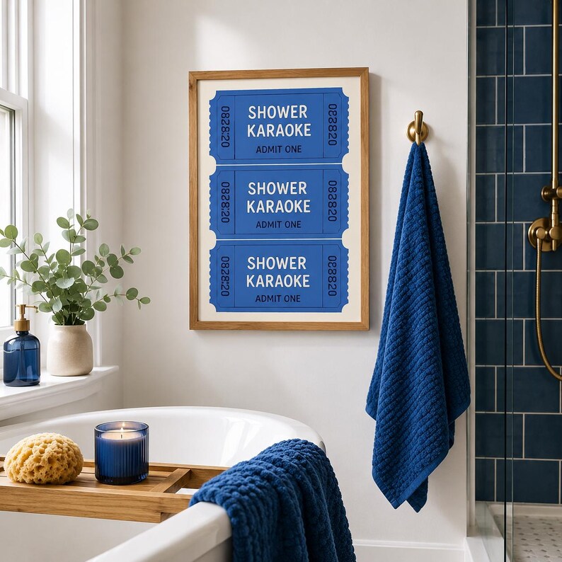 Op de afbeelding: Een ingelijste wandprint met drie gestapelde blauwe toegangskaartjes met witte tekst die SHOWER KARAOKE ADMIT ONE leest en het nummer 082820 aan de zijkanten. De print is ingelijst in een lichthouten lijst aan een witte muur.
