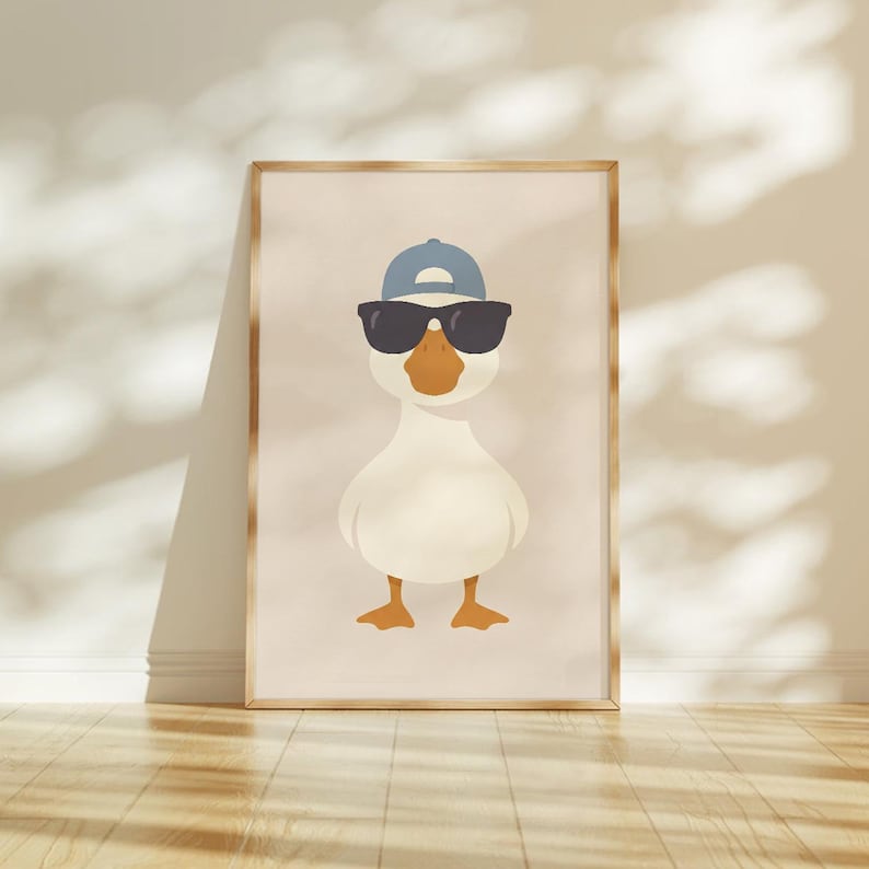 May include: A framed print featuring a cartoon duck wearing sunglasses and a blue baseball cap. The duck has a white body, orange beak and feet, and is set against a neutral background. The artwork is displayed in a wooden frame.