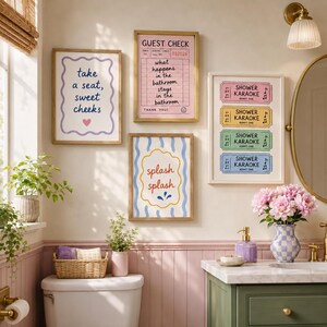 May include: Four framed wall art prints displayed in a bathroom. One print features a guest check design with text, another shows four colorful shower karaoke tickets, one says take a seat sweet cheeks with a heart, and one says splash splash.